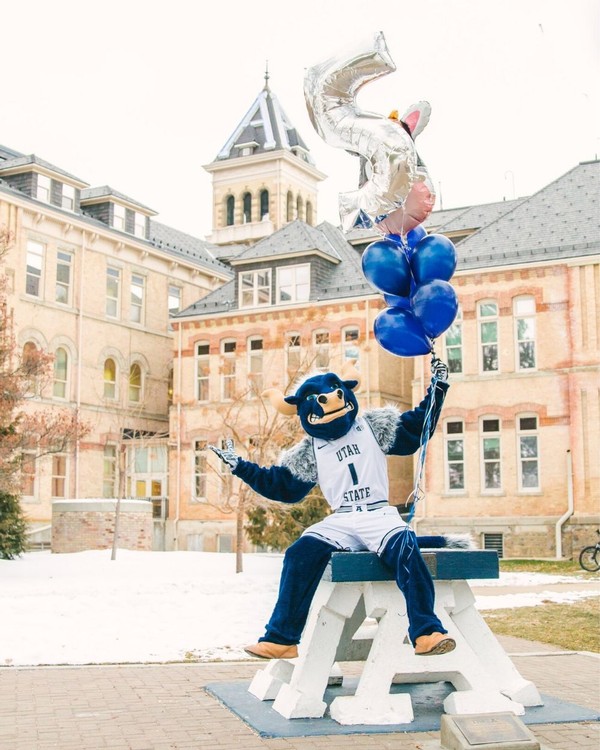 USU mascot Big Blue holds balloons atop the Block A in front of Old Main